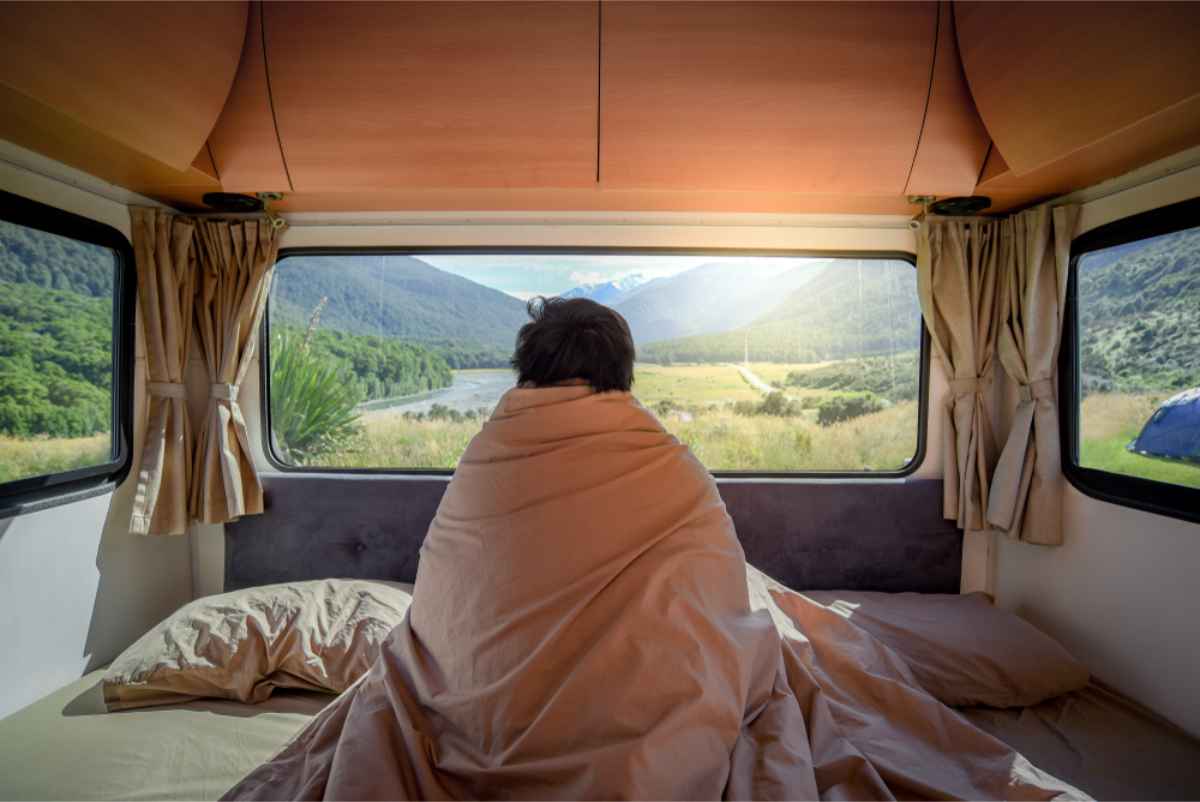 Tourist covered in his camper blanket enjoying the views from the rear of his campervan