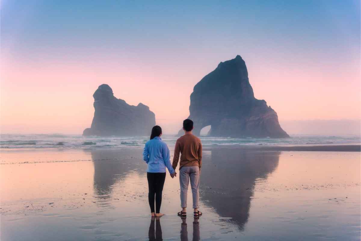 couple standing before an impresive beach in NZ at dawn
